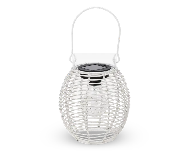 Ovalformet lanterne med hvidt flettet rattan-udvendigt og et solidt håndtag til ophængning. Toppen har et sort solpanel, hvilket indikerer, at den er solcelledrevet. Indeni ses en klar pære, der udsender lys, når den er opladet. Den åbne fletning lader lyset skinne igennem og skaber dekorative mønstre.