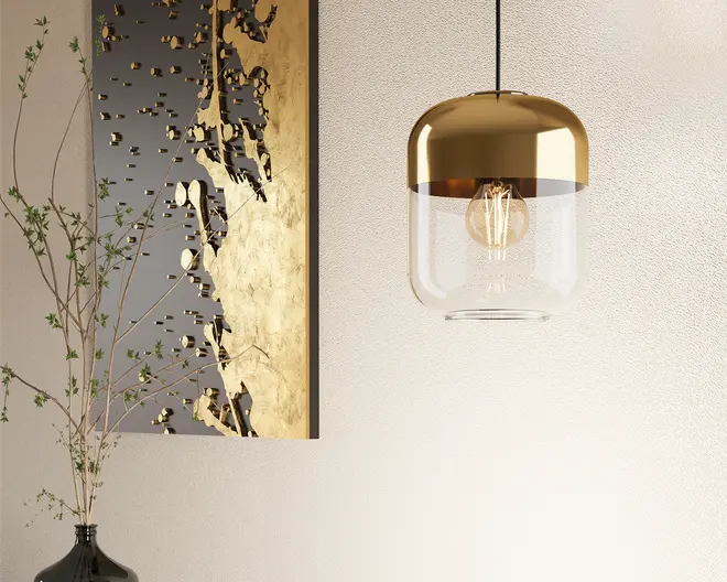 Loftlampe med et moderne design, der har en rund, metallisk gylden top og en klar glasbund. Pæren er synlig indeni, hvilket bidrager til det nutidige udtryk. Lampen hænger fra en sort ledning, og det samlede udseende er stilrent og elegant, velegnet til moderne indretning.