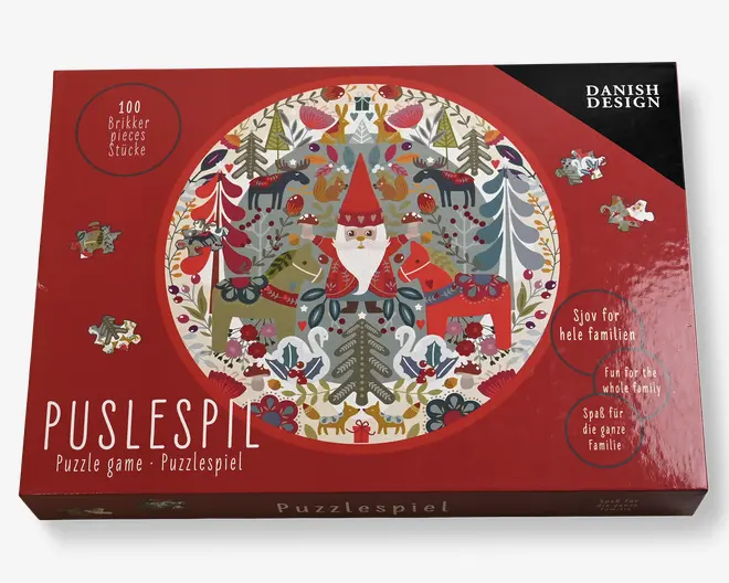 Æsken har en festlig, cirkulær illustration med en nisse i rød hue og frakke i midten, omgivet af stiliserede skovdyr som hjorte, ræve, svaner og fugle samt træer og dekorative elementer i røde, grønne og hvide nuancer. Puslespillet består af 100 brikker og har et skandinavisk design. Emballagen fremhæver, at det er sjovt for hele familien og understreger det danske design.