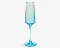 Et højt, slankt glas med sekskantet fod og lang stilk, der har en blå farvegradient, som går fra dyb blå i bunden til gennemsigtig ved kanten. Glasset har et moderne, geometrisk design med rene linjer og en glat overflade.