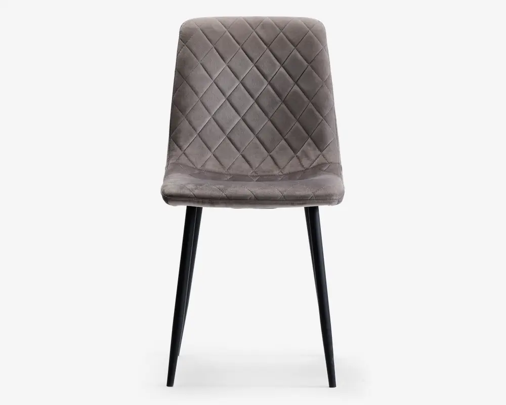 Stol med polstret sæde og ryglæn betrukket med blødt, gråt velourstof. Ryglænet og sædet har et quiltet design med diamantmønster, som giver ekstra struktur og stil. Stolen står på fire slanke, sorte metalben, der smalner let ind mod gulvet og giver et moderne og elegant udtryk.