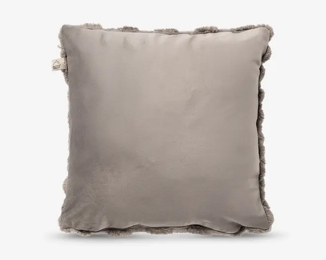 Firkantet beige pude med glat, ensfarvet midte og blød flæsekant hele vejen rundt samt en lille stofetiket i siden.