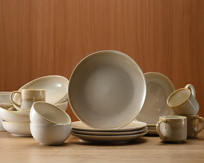 Et koordineret sæt keramikservice i afdæmpede beige og cremefarver med let plettet, mat finish. Sættet indeholder middagstallerkener, skåle og krus, alle med blødt afrundede kanter og et minimalistisk design. Krusene har brede, behagelige hanke, og skålene er dybe nok til suppe eller morgenmad. Det samlede udtryk er moderne og varmt, velegnet til både hverdags- og festbrug.