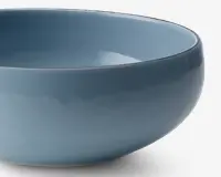 En glat, rund skål med en blank lyseblå overflade. Skålen har et enkelt, moderne design med blødt buede sider og ensartet farve over det hele. Kanten er let afrundet, og overfladen ser reflekterende ud, hvilket tyder på, at den er lavet af glaseret keramik.