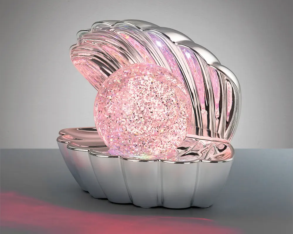 En dekorativ lampe formet som en åben muslingeskal med en blank, sølvfarvet overflade. Inde i skallen ligger en stor, rund kugle med tekstur, der udsender et blødt lyserødt skær med glitrende detaljer, hvilket skaber en glitrende effekt. Lampen har et moderne, fantasifuldt design og egner sig som et iøjnefaldende element i boligindretningen.
