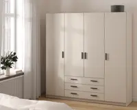 Et moderne, fritstående garderobeskab med mat beige finish. Skabet har fire høje låger med slanke, sorte rektangulære greb samt tre rummelige skuffer nederst i midten, alle med matchende sorte greb. Garderobeskabet har et rent, minimalistisk design og står direkte på gulvet. Øverst på skabet står en rund, grå opbevaringsboks.