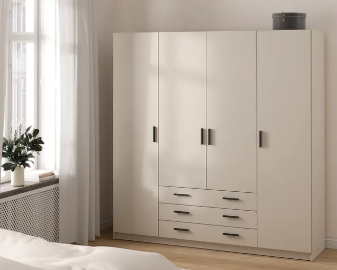 Et moderne, fritstående garderobeskab med mat beige finish. Skabet har fire høje låger med slanke, sorte rektangulære greb samt tre rummelige skuffer nederst i midten, alle med matchende sorte greb. Garderobeskabet har et rent, minimalistisk design og står direkte på gulvet. Øverst på skabet står en rund, grå opbevaringsboks.