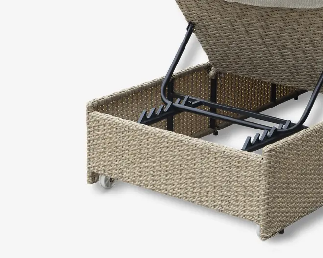 Nærbillede af et opbevaringsrum med hængslet låg, fremstillet af lysebeige syntetisk rattan. Låget er delvist åbent og afslører et rummeligt indre understøttet af en robust sort metalramme. Rummet har glatte, afrundede hjørner og er udstyret med små hjul for nem mobilitet.