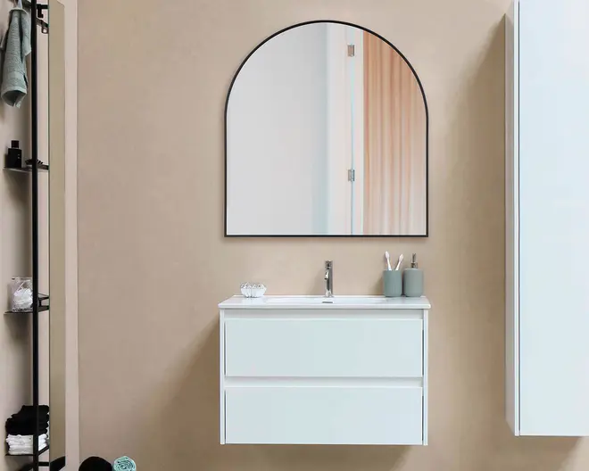 Et moderne badeværelsesmøbel med et minimalistisk design, bestående af et væghængt, hvidt skab med to grebsfri skuffer, en rektangulær integreret vask og en slank krom vandhane. Over møblet hænger et stort, buet spejl med en tynd sort ramme. På bordpladen står en lille glasskål samt to matchende beholdere med tandbørster og andre badeværelsesartikler. Bagvæggen er i en neutral beige farve, hvilket bidrager til det rene og moderne udtryk.