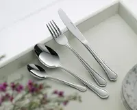 Fire stykker blankt bestik i rustfrit stål ligger på en lys bakke: en middagskniv, middagsgaffel, spiseske og teske. Hvert stykke har et klassisk, let dekorativt håndtag med bløde kurver og en udsmykket kant nær enden. Overfladerne er meget blanke, og stilen er elegant og egnet til både hverdag og fest.
