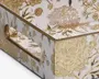 Nærbillede af et hjørne af en æske med en blank hvid overflade, dekoreret med indviklede guldfarvede blomster og detaljer. Blomsterne er præget, hvilket giver en tekstureret, hævet effekt, og nogle kronblade har et diskret lavendelfarvet skær. Æsken har et matchende håndtag med samme guldfarvede blomstermønster, og det samlede udtryk er luksuriøst og dekorativt.