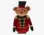 Bamse med blød, lysebrun pels iført en festlig soldateruniform. Uniformen består af en rød velourjakke med guldfarvede kanter, grønne detaljer og dekorative guldknapper. Bamsen har en matchende høj grøn og rød hat samt arme og ben dækket af rødt og grønt stof med gulddetaljer. Ansigtet er venligt og broderet.