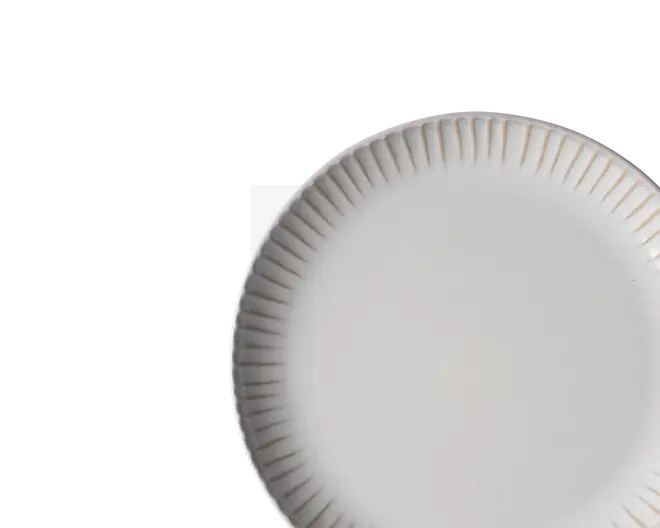 Enkel hvid rund tallerken med rillet, bølget kant og glat midte, vist delvist beskåret på sort baggrund.