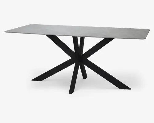 Rektangulært bord med en glat, lysegrå bordplade i sten eller stenlook. Bordpladen har rene, lige kanter og et moderne udtryk. Understellet består af et markant sort metaldesign med flere skrå ben, der mødes i midten og danner en stjerne- eller edderkoplignende form, hvilket giver både stabilitet og et iøjnefaldende udseende.