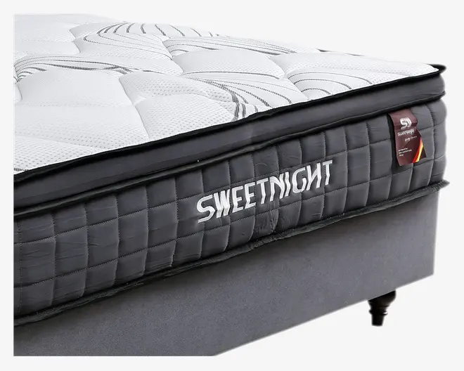 Nærbillede af en tyk, blød madras med quiltet hvid og grå top, der har diskrete swirl-mønstre. Siderne er mørkegrå med et ternet, polstret udseende og mærket 'SWEETNIGHT' broderet i hvidt. Madrassen har et tydeligt, ekstra komfortlag øverst og står på en enkel, grå sengebund med korte, mørke ben.