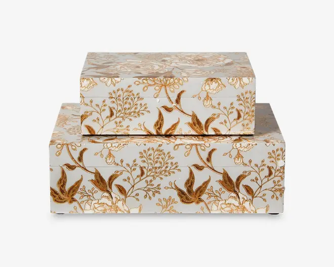 Sæt med to rektangulære æsker med hvid baggrund, dekoreret med et indviklet guld- og brunt blomstermønster. Æskerne kan stables, hvor den mindre æske er placeret oven på den større. Begge æsker har en glat, blank overflade og detaljerede botaniske motiver med blade og blomster, hvilket giver dem et elegant og dekorativt udseende.