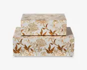 Sæt med to rektangulære æsker med hvid baggrund, dekoreret med et indviklet guld- og brunt blomstermønster. Æskerne kan stables, hvor den mindre æske er placeret oven på den større. Begge æsker har en glat, blank overflade og detaljerede botaniske motiver med blade og blomster, hvilket giver dem et elegant og dekorativt udseende.