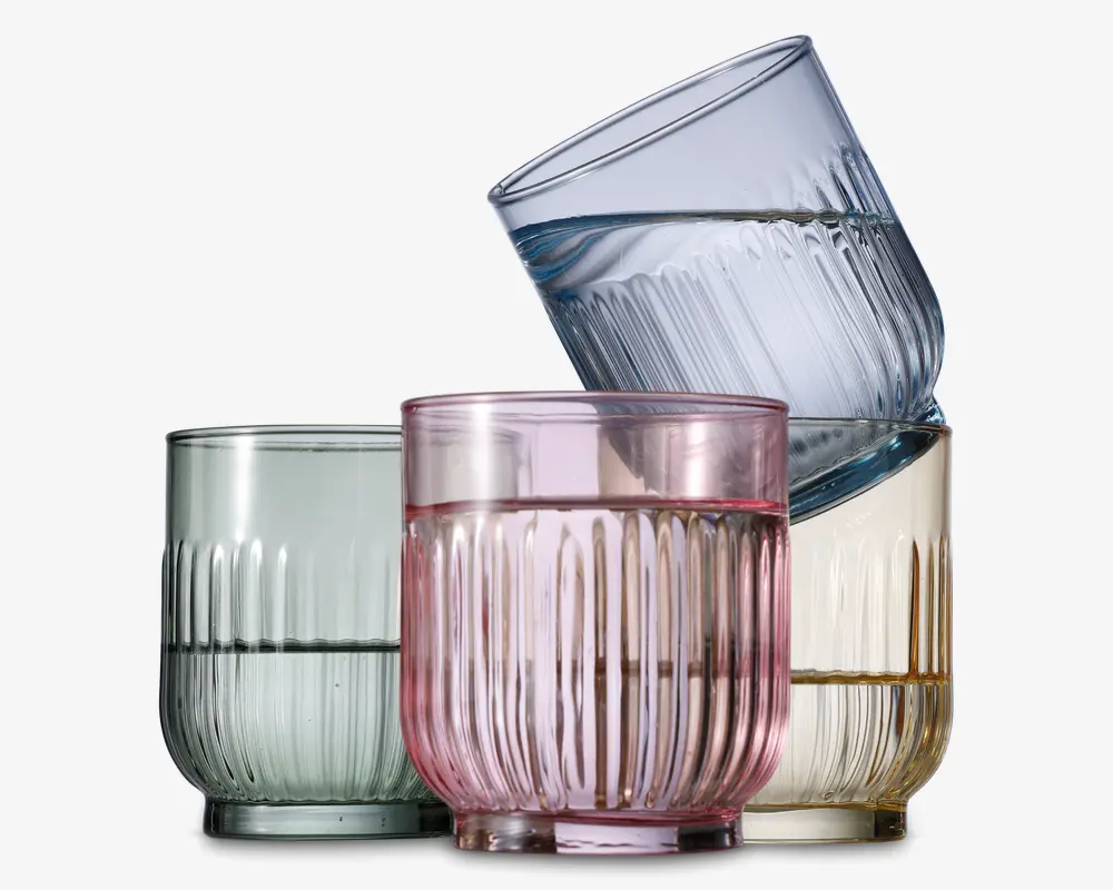 Sæt med fire lave drikkeglas, hver med rillet tekstur og en let rundet form. Glassene har forskellige transparente farver: lysegrøn, pink, gul og blå. Designet har lodrette riller, hvilket giver et stilfuldt og moderne udtryk.