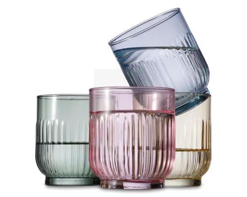 Sæt med fire lave drikkeglas, hver med rillet tekstur og en let rundet form. Glassene har forskellige transparente farver: lysegrøn, pink, gul og blå. Designet har lodrette riller, hvilket giver et stilfuldt og moderne udtryk.