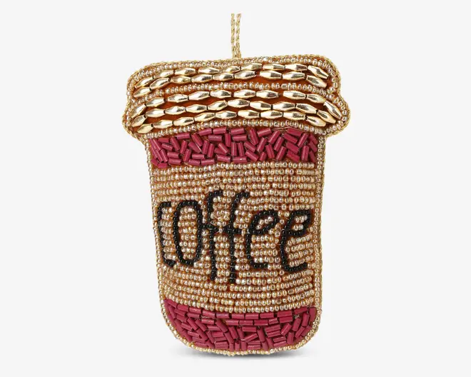 Udsmykket accessory formet som en to-go kaffekop, dekoreret med guld-, bronze- og bordeauxfarvede perler. Låget har skinnende guld ovale perler, mens kroppen er dækket af små runde perler med ordet 'coffee' stavet med sorte perler. Top- og bundkanterne er fremhævet med bordeaux cylindriske perler for ekstra struktur.