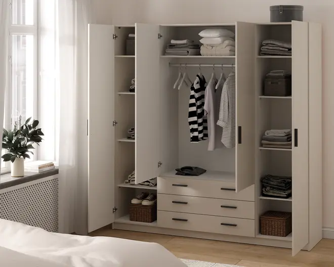 Rummeligt garderobeskab med moderne, minimalistisk design i en lys beige farve. Skabet har fire låger, flere justerbare hylder, en central bøjlestang med flere bøjler samt tre store skuffer nederst. Garderoben er organiseret med sammenlagte tøjstykker, kurve, sko og opbevaringskasser, hvilket giver rigelig opbevaringsplads til forskellige ting.