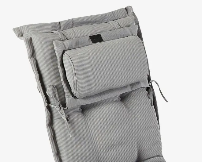 Nærbillede af en polstret, lysegrå hynde med diskret stribet tekstur. Hynden har en tyk, justerbar nakkepude, der er fastgjort med stofløkker og bindebånd, samt ekstra bindebånd i siderne til fastgørelse på en stol. Overfladen ser blød og komfortabel ud med synlige syninger og lette indsyninger for ekstra støtte.