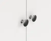 Et par runde greb i børstet metal med en glat, let buet overflade og en kort cylindrisk stilk, monteret på en hvid skabslåge. Grebene har en mat eller satin nikkel-finish, hvilket giver et moderne og diskret udtryk.