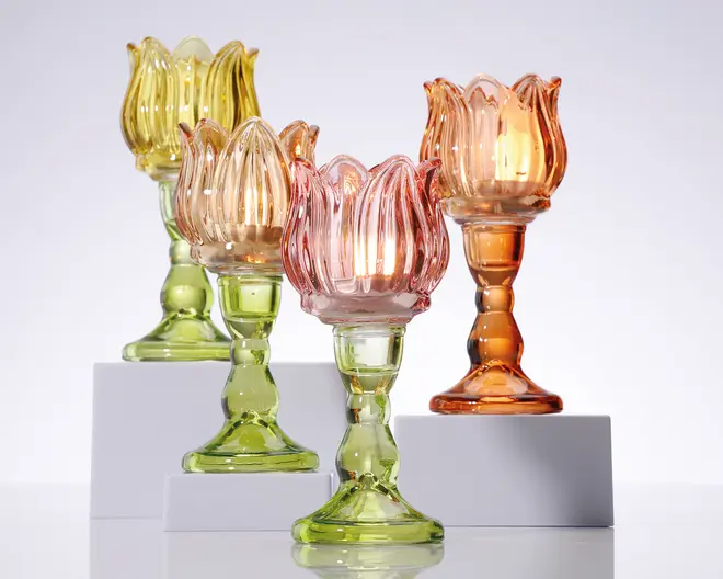 Sæt med fire dekorative lysestager i glas med tulipanformet design. Hver lysestage har en riflet, kronbladslignende kant og en solid, rund fod. Farverne omfatter gennemsigtig gul, pink, orange og grøn, hvilket giver et livligt og elegant udtryk. Glasset er tykt og blankt, og reflekterer lyset smukt. Perfekt til at tilføje farve og elegance til ethvert miljø.