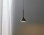 En moderne pendellampe med en mat sort, kegleformet skærm, der hænger fra en tynd sort ledning. Lampen er tændt og udsender et blødt lys nedad. Designet er minimalistisk og stilrent, velegnet til moderne indretning.