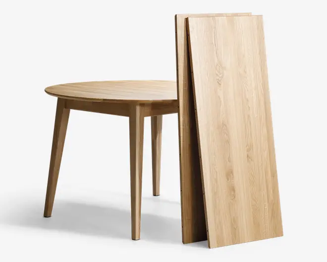 Bord i lyst træ med glat, naturlig finish og koniske ben. Bordet er vist delvist samlet, med to ekstra tillægsplader stående oprejst ved siden af, hvilket viser, at bordet kan forlænges for ekstra siddepladser eller bordplads. Træets åretegning er synlig og giver et moderne, men varmt udtryk.