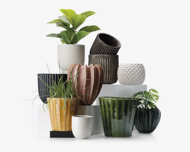 Et udvalg af dekorative urtepotter i forskellige former, størrelser og farver. Potterne har forskellige teksturer, herunder riflede, blanke, matte og piggede overflader. Farverne spænder fra hvid, sort og brun til gul, grøn og lyserød. Nogle potter har lodrette riller, mens andre har en glat eller mønstret finish. Flere potter indeholder grønne planter, hvilket viser deres anvendelse til indendørs dekoration.