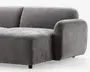 Billedet viser en del af en moderne sofa med blødt, velouragtigt gråt stof. Sofaen har en kraftig, afrundet armlæn og en bred, dyb siddepude, som giver god komfort. Ryglænet er let buet, og designet er minimalistisk med glatte, rene linjer. Sofaen står på korte, solide ben, som næsten ikke kan ses.
