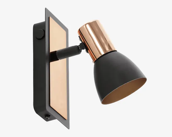 Væghængt spotlampe med en mat sort, konisk lampeskærm og en metallisk kobberdetalje øverst. Lampen har en rektangulær bagplade med en kobberfarvet indsats og sort ramme. Lampens hoved kan justeres, så lyset kan rettes i forskellige retninger.