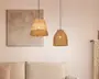 To hængelamper med håndvævede lampeskærme af naturfibre hænger fra loftet. Lampen til venstre har en konisk form med skiftevis lyse og mellembrune bånd, mens lampen til højre har en rund, klokkeformet skærm i ensartet lysebrun farve. Begge skærme har en tekstureret, rustik overflade, og ledningerne er tynde og sorte. Lamperne udsender et varmt, blødt lys, der understreger rummets hyggelige og indbydende stemning.