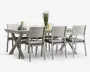 Rektangulært spisebordssæt med lys grå finish, bestående af seks matchende stole og to bænke. Stolene har vandrette lamelrygge og er udstyret med grå sædehynder for ekstra komfort. Bordet har solide krydsede ben for stabilitet. På bordpladen står der stablede tallerkener, kopper, en gul kande og en dekorativ vase med hvide blomster, hvilket giver et elegant udtryk til opstillingen.