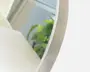 Nærbillede af et rundt spejl med en elegant, børstet metalramme. Spejlet reflekterer et lyst rum med et vindue og nogle grønne planter, hvilket antyder et moderne og luftigt interiør. Rammen har en glat overflade og en diskret metallisk glans.