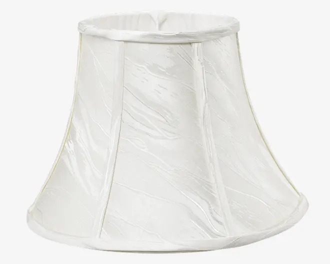 En klokkeformet lampeskærm lavet af hvidt stof med en diskret krøllet tekstur. Skærmen har lodrette stofpaneler adskilt af smalle bånd, og både øverste og nederste kant er afsluttet med en glat, afrundet stofkant. Udtrykket er klassisk og elegant, velegnet til traditionel eller tidløs indretning.