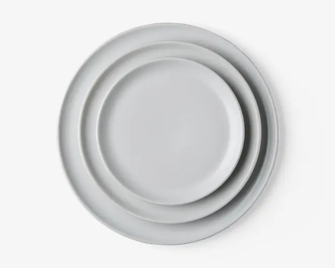 Tre runde tallerkener i forskellige størrelser stablet oven på hinanden, alle med en glat, ensfarvet hvid overflade og en let forhøjet kant. Designet er minimalistisk og moderne, velegnet til forskellige borddækninger.