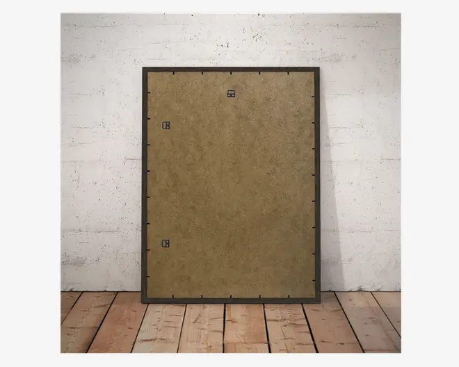 Billedet viser bagsiden af en rektangulær ramme med en brun MDF-bagside. Rammen har en mørk kant og er udstyret med tre metalophæng, så den kan hænges både lodret og vandret på væggen. Bagsiden holdes fast med flere sorte clips langs kanterne. Rammen står oprejst mod en hvid, tekstureret væg på et trægulv.