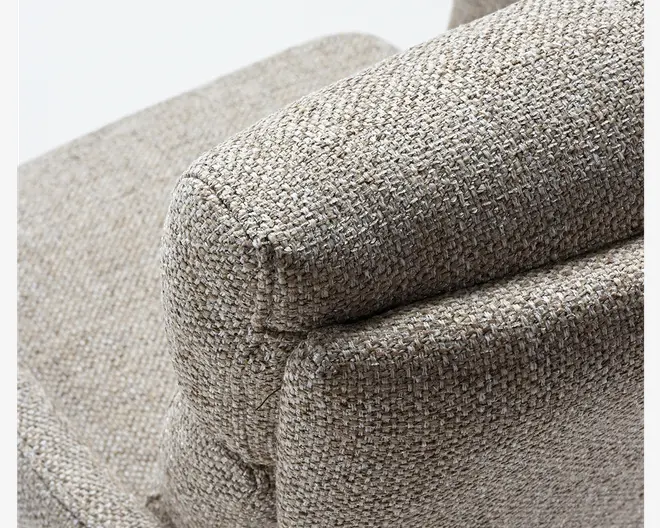 Nærbillede af et møbelarmlæn betrukket med en tekstureret, vævet beige stof. Materialet har en grov vævning, hvilket giver det et naturligt og let rustikt udseende. Armlænet er tykt polstret med synlige sømme, der markerer formen, hvilket indikerer komfort og holdbarhed.