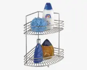 Et to-etagers hjørneformet brusehylde i metal med kromfinish. Hylden har åbne trådhylder og forhøjede kanter, der forhindrer, at ting falder ud. Den er designet til at passe ind i et hjørne og udnytter pladsen optimalt, med god afstand mellem hylderne til høje flasker. Billedet viser hylden med forskellige badeprodukter for at illustrere opbevaringsmulighederne.