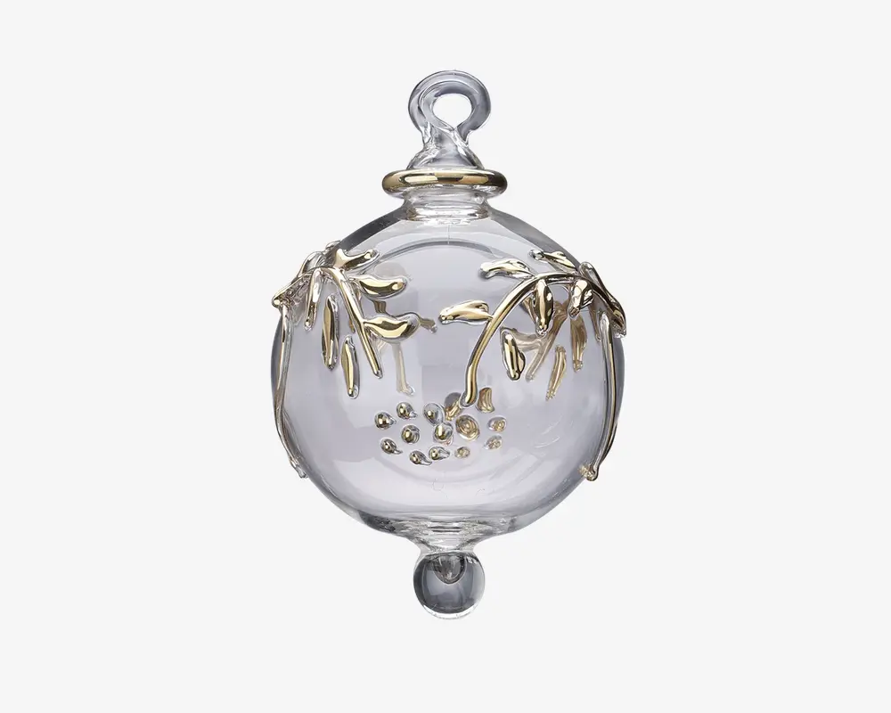 En klar, kugleformet glaspynt med en løkke øverst til ophængning. Overfladen er dekoreret med fine grene og blade i guldfarve samt små guldfarvede prikker samlet i en klynge. Pynten har en glat, blank finish og en lille rundet udvidelse i bunden.