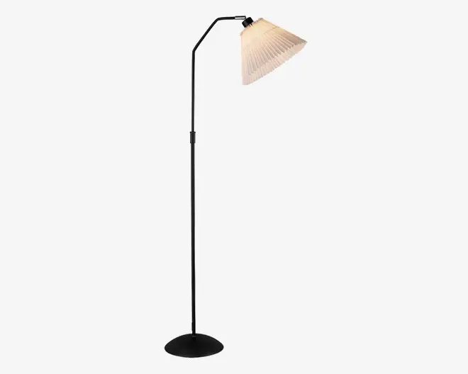 Høj gulvlampe med en slank, kromfarvet metalstang og rund, sort fod. Lampen har en vinklet arm øverst, der holder en plisseret, råhvid stofskærm, som giver et blødt og diffust lys. Designet er moderne og minimalistisk, velegnet til nutidige indretninger.