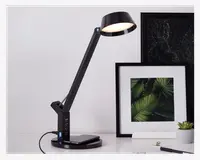 Elegant sort skrivebordslampe med justerbar arm og rund lampeskærm, udstyret med touch-kontrolpanel på basen. Basen har flere USB-opladningsporte og en trådløs opladningsplade til enheder. Lampen har et moderne, minimalistisk design, der passer til både kontor og hjem.