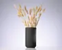 En høj sort cylindrisk vase med lodret rillet struktur, fyldt med en buket tørrede beige græsstrå med bløde, fjeragtige aks.