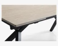Nærbillede af et bordhjørne med en lys træstruktur bordplade med en glat, mat overflade. Bordpladen har en let skrå kant og hviler på en solid, sort metalramme med skrå ben, hvilket giver et moderne og industrielt udtryk.