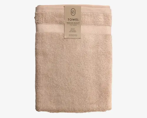 Et pænt sammenfoldet, beige håndklæde lavet af 100% bomuld. Håndklædet har en blød, fyldig tekstur med et dekorativt bånd nær den ene ende, som giver et diskret designelement. Mærket angiver, at det er af premium kvalitet, måler 70 x 140 cm og er en del af en essentials-kollektion. Kanterne er pænt syet for ekstra holdbarhed.