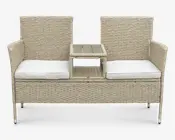 Udendørs bænk med to separate siddepladser, hver med høj ryg og armlæn. Bænken er lavet af lysebeige flettet rattan og har tykke, hvide sædehynder for ekstra komfort. Mellem sæderne er der et hævet centralt bord med en flad overflade, velegnet til at placere drikkevarer eller småting, samt en åben hylde nedenunder til ekstra opbevaring.