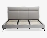 Moderne sengegavl med en høj, rektangulær polstret hovedgavl i lysegråt stof, med diskrete lodrette og vandrette syninger, der giver et paneludseende. Rammen har rene linjer og er også polstret i matchende lysegråt stof. Bunden har jævnt fordelte lameller af træ til støtte for madrassen, og sengen står på skråtstillede sorte ben for et moderne udtryk.