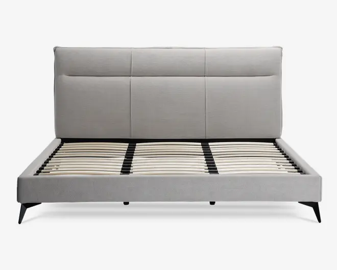 Moderne sengegavl med en høj, rektangulær polstret hovedgavl i lysegråt stof, med diskrete lodrette og vandrette syninger, der giver et paneludseende. Rammen har rene linjer og er også polstret i matchende lysegråt stof. Bunden har jævnt fordelte lameller af træ til støtte for madrassen, og sengen står på skråtstillede sorte ben for et moderne udtryk.